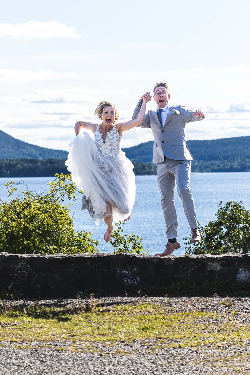Brudpar som hoppar från en stenmur, med sjö och berg bakom