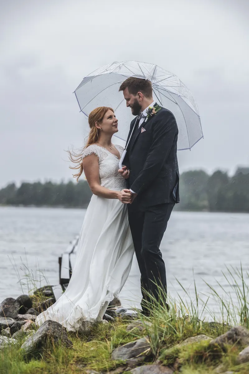 Brudpar under ett genomskinligt paraply vid en sjö