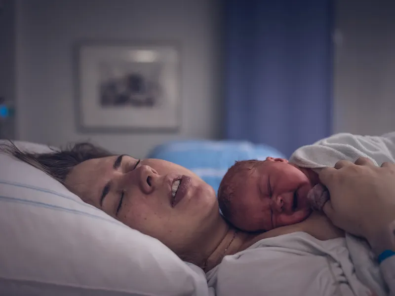 Mamma med sin nyfödda på bröstet i en sjukhussäng
